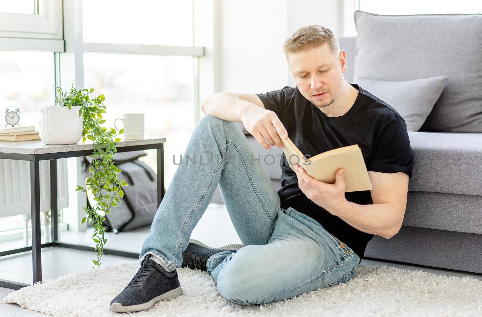 Attractive man reading paper book sitting on floor at home
