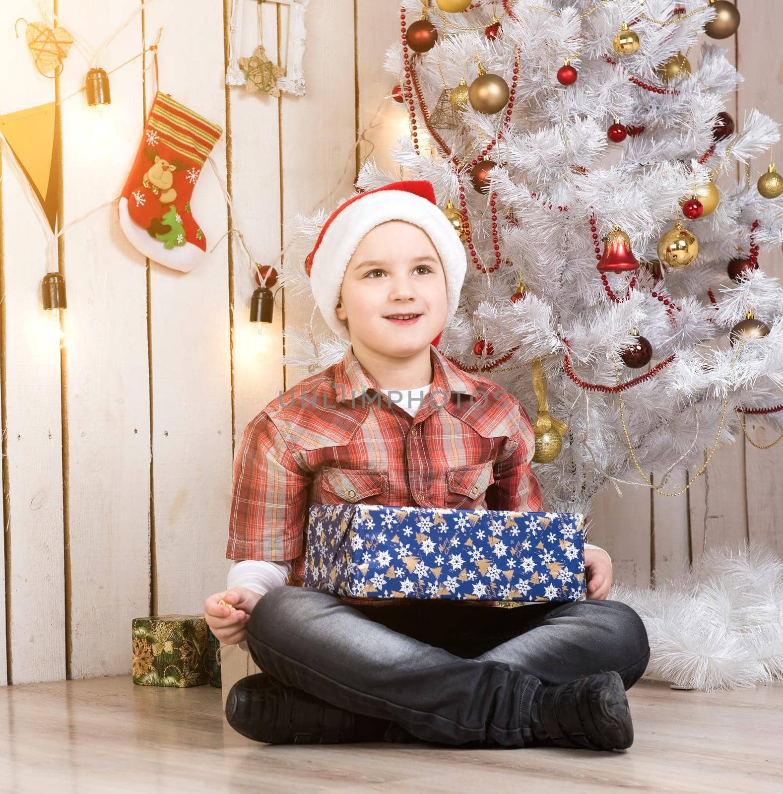 little boy in red hat taking present box near new year tree in decorated room
