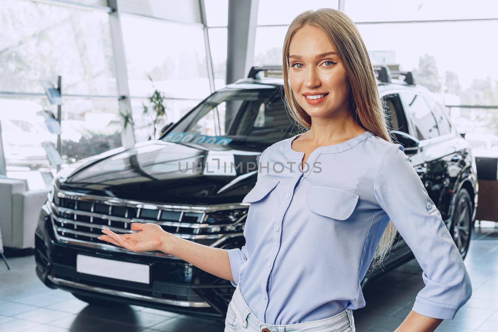 Attractive young female car dealer standing in showroom near a new car