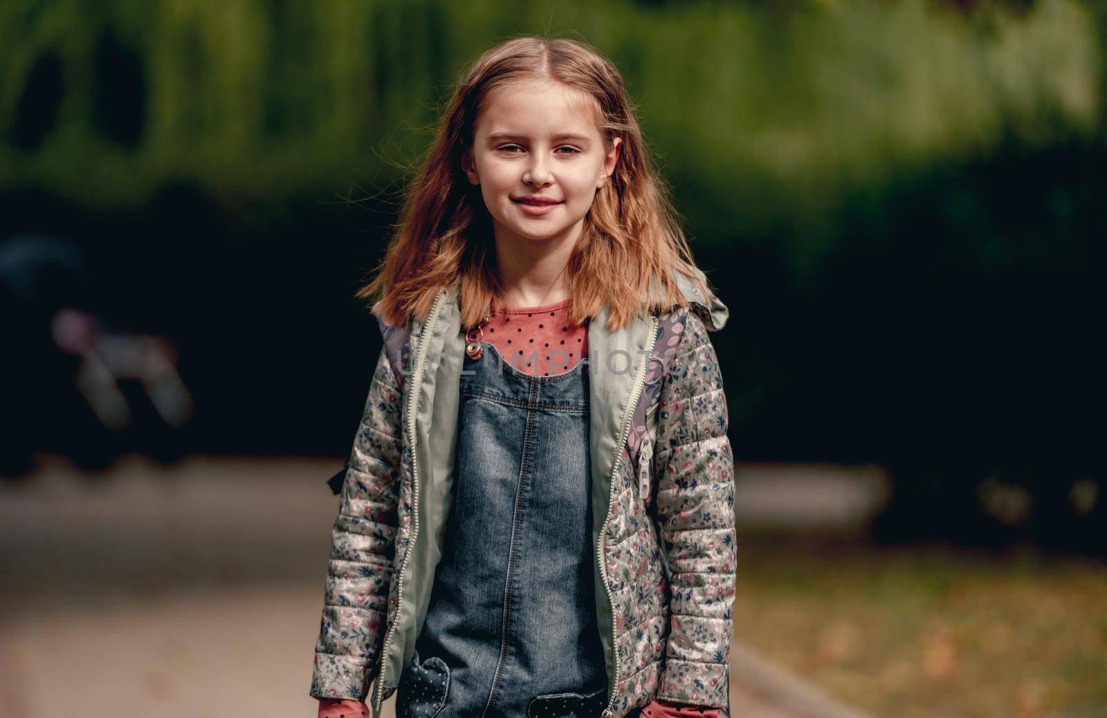 Pretty school girl in autumn park portrait. Beautiful primary school female pupil kid outdoors