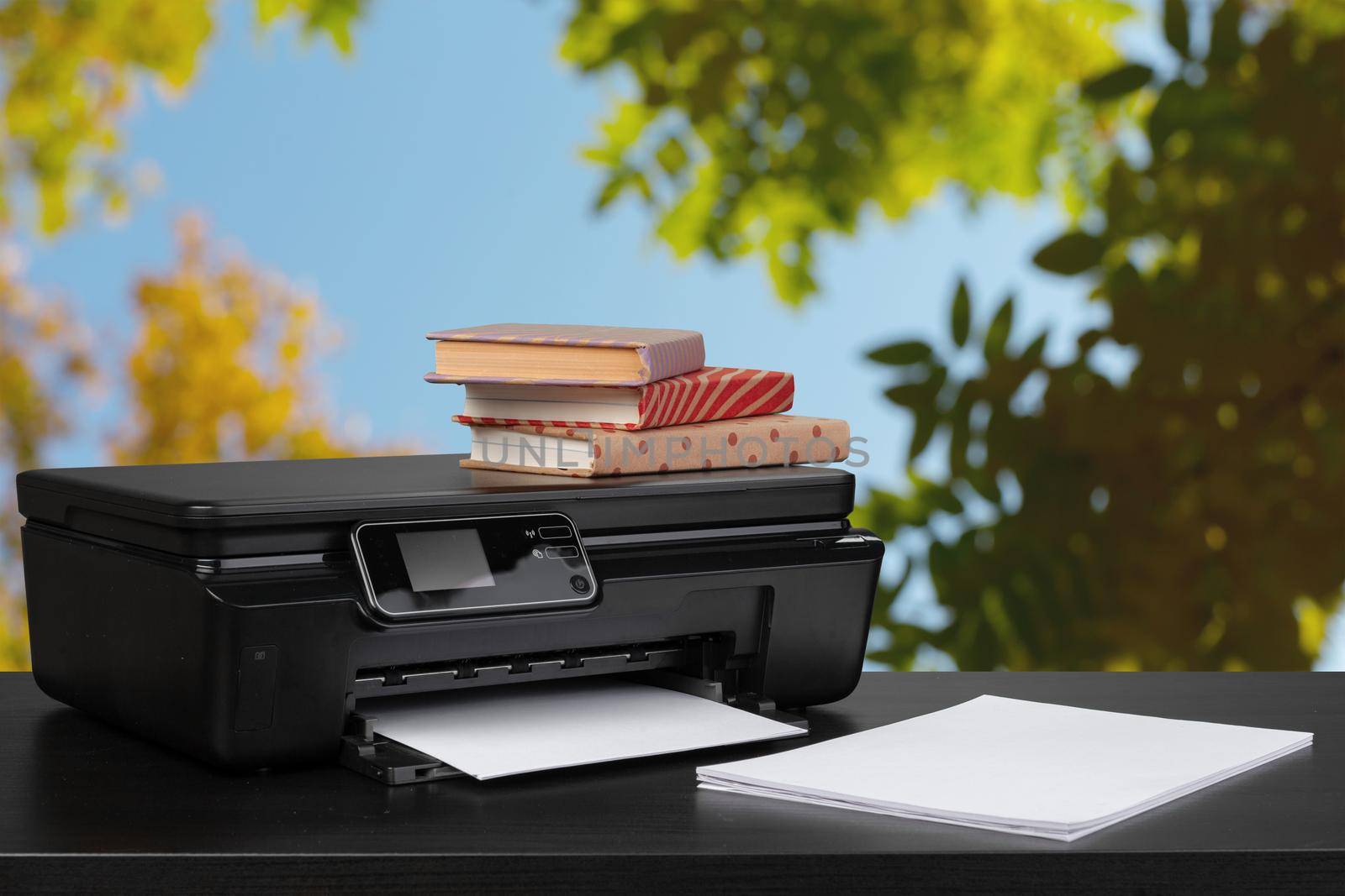 Stack of books and home printer against blurred background, close up