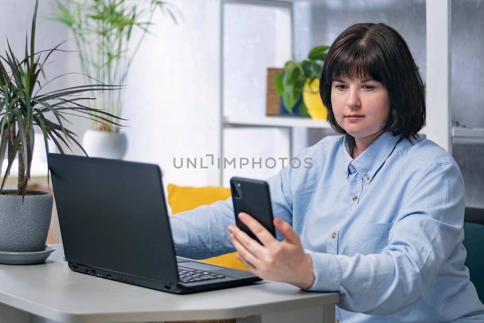 Young woman is working at her workplace. Business woman with laptop and phone in hand.