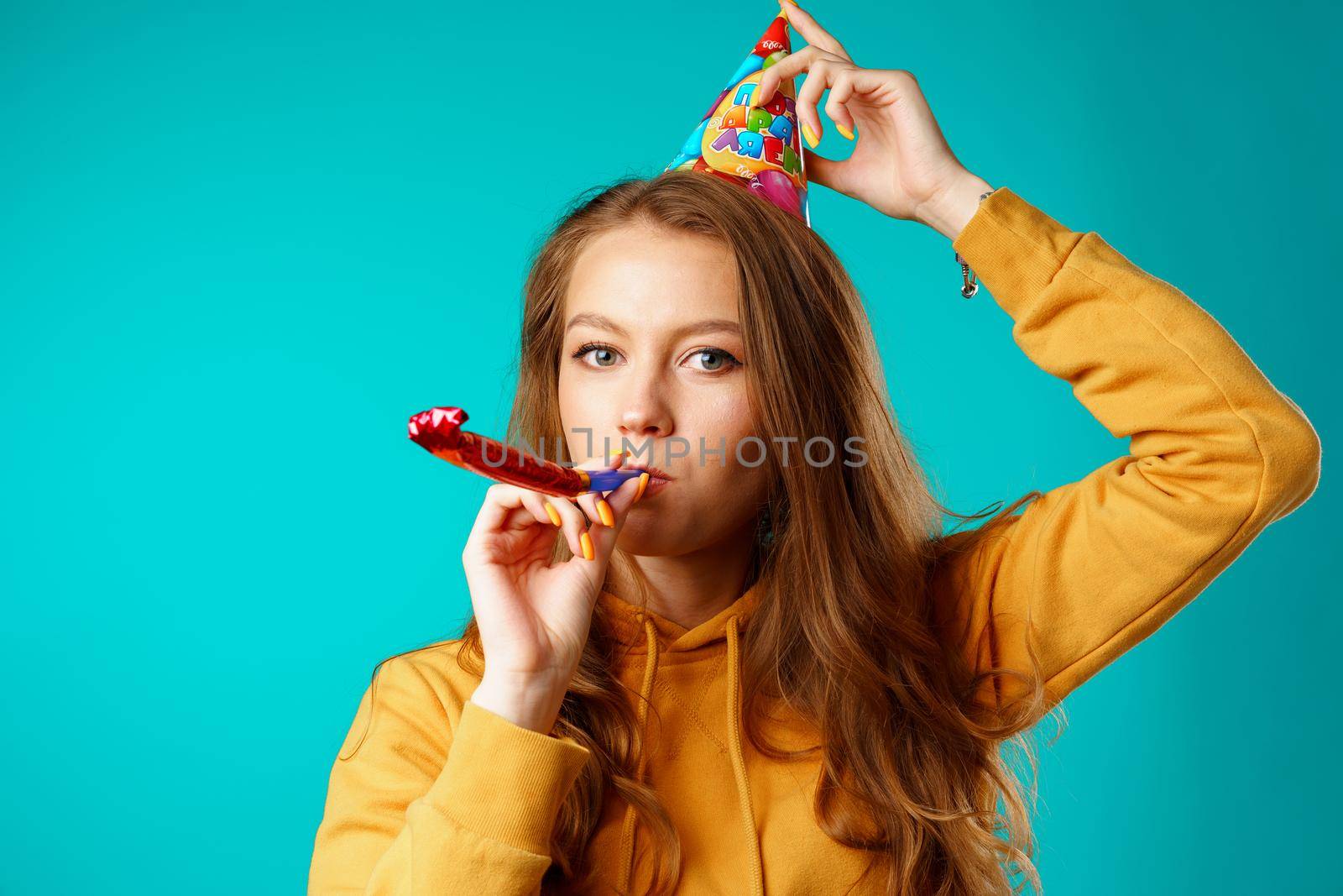Young casual woman in party cone with horn against blue background