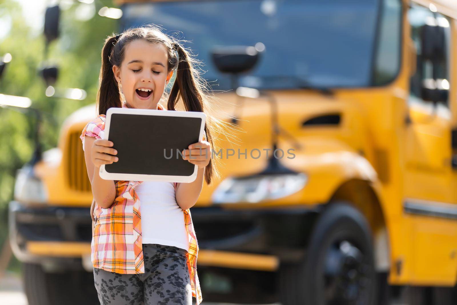 adorable little schoolgirl near school bus and looking at camera