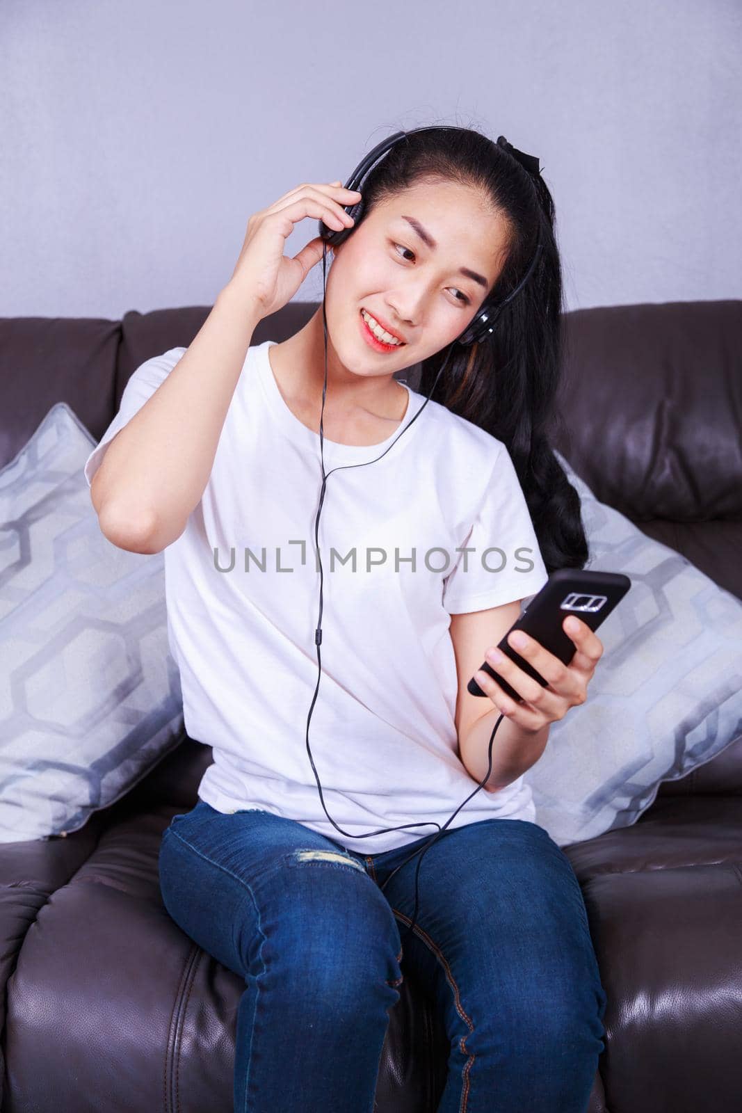 young woman listening to music in headphones with moblie on sofa at home