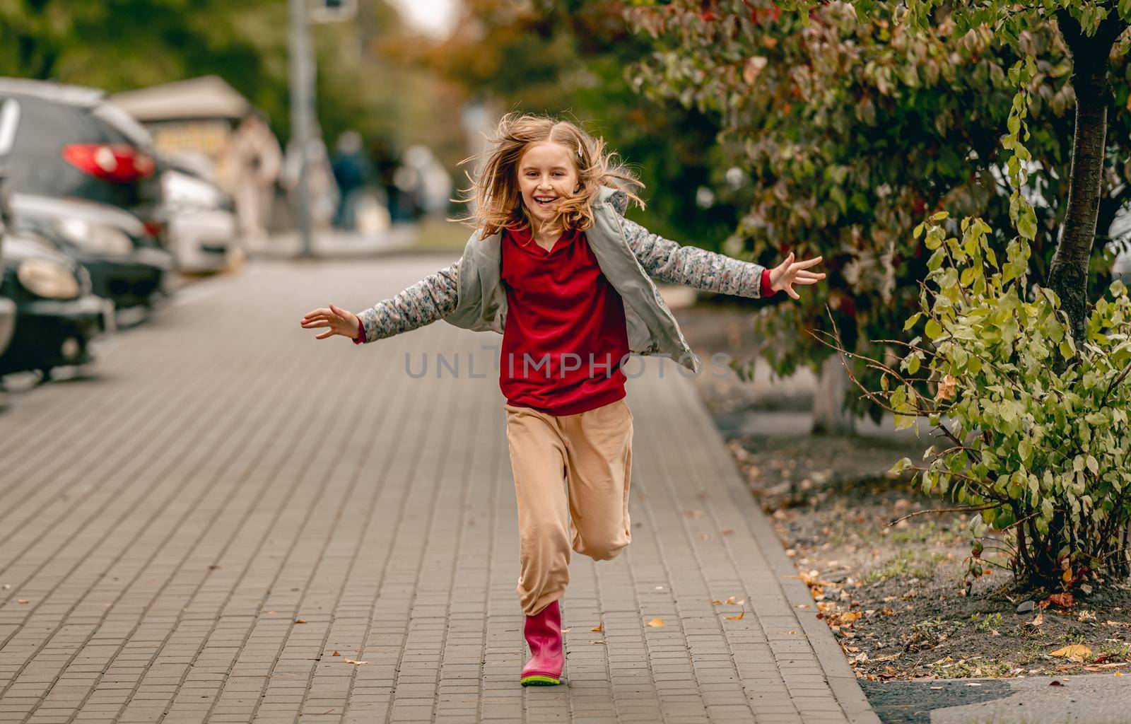 Preteen girl wearing rubber boots running at autumn at street. and smiling Pretty female kid in gumboots outdoors