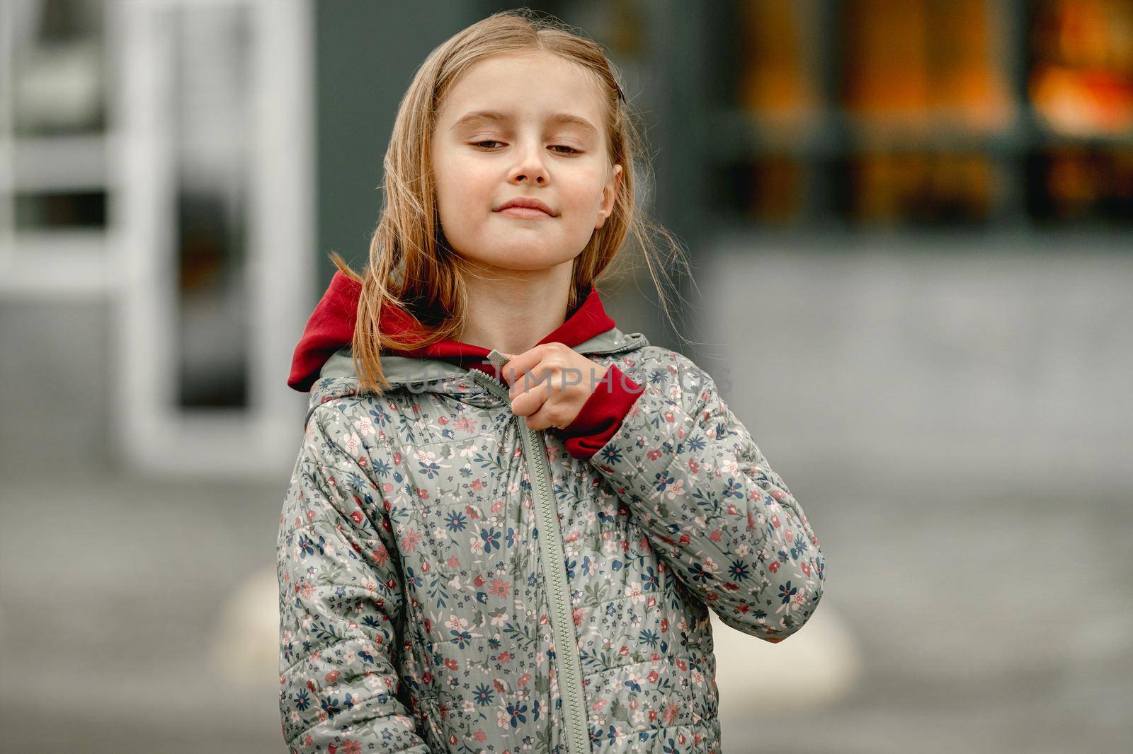 Pretty girl kid autumn portrait outdoors. Preteen female child closes coat at the street