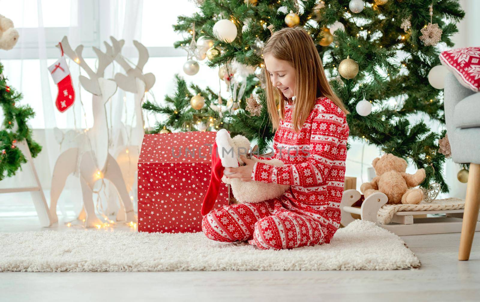 Pretty child girl open Christmas red gift box at home with traditional decorated tree. Kid celebrating New Year with presents