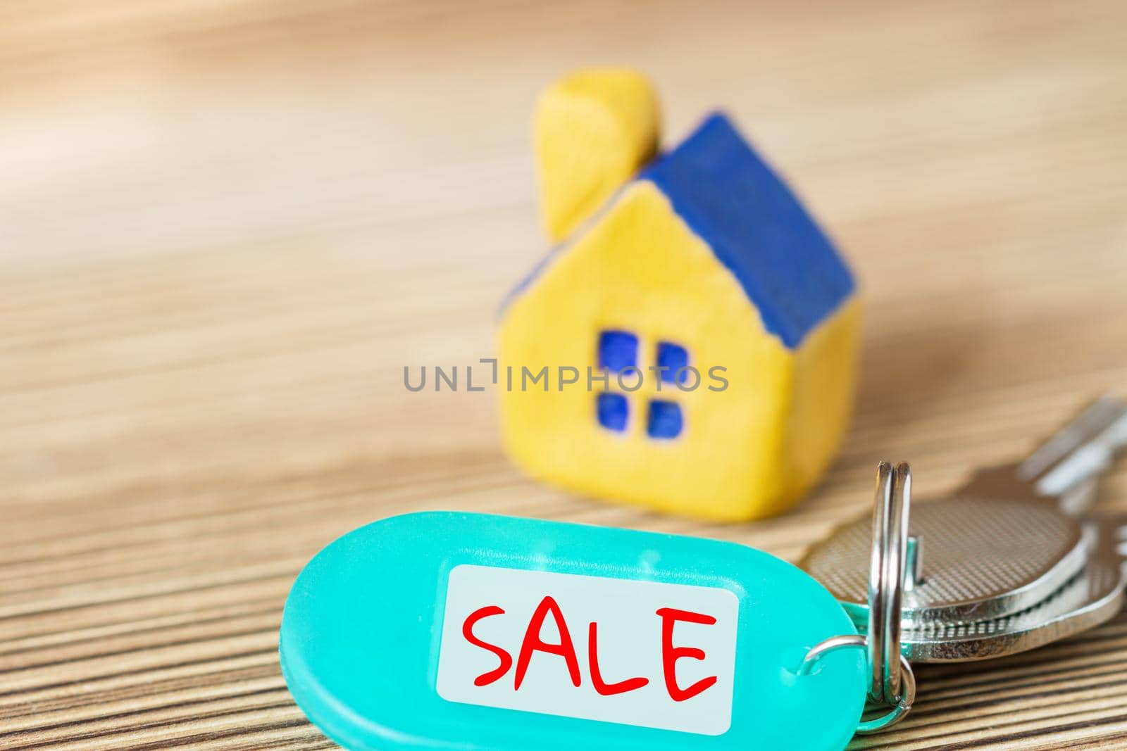 Miniature yellow toy house with keys and inscription SALE on the wooden surface. Property and real estate concept. Selective focus