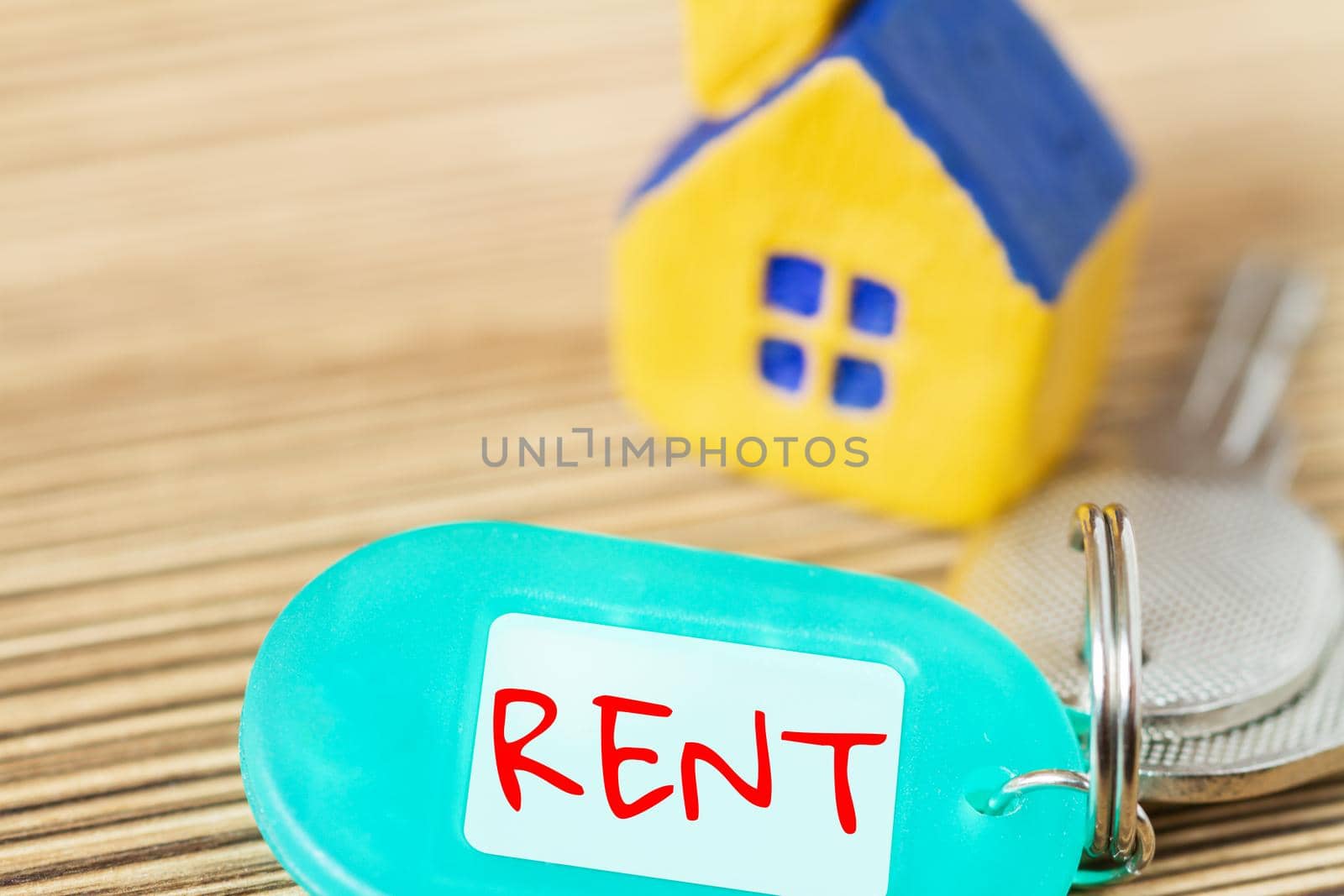 Miniature yellow toy house with keys and inscription RENT on the wooden surface. Property and real estate concept. Selective focus