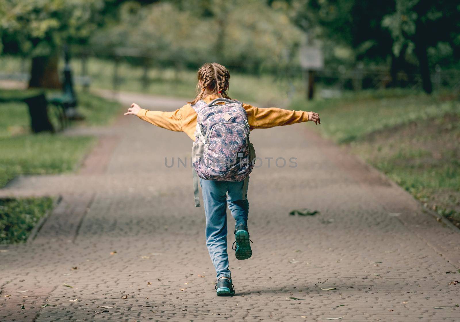 Preteen school girl with backpack running in the park after lessons portrait from back. Carefree child kid at autumn outdoors