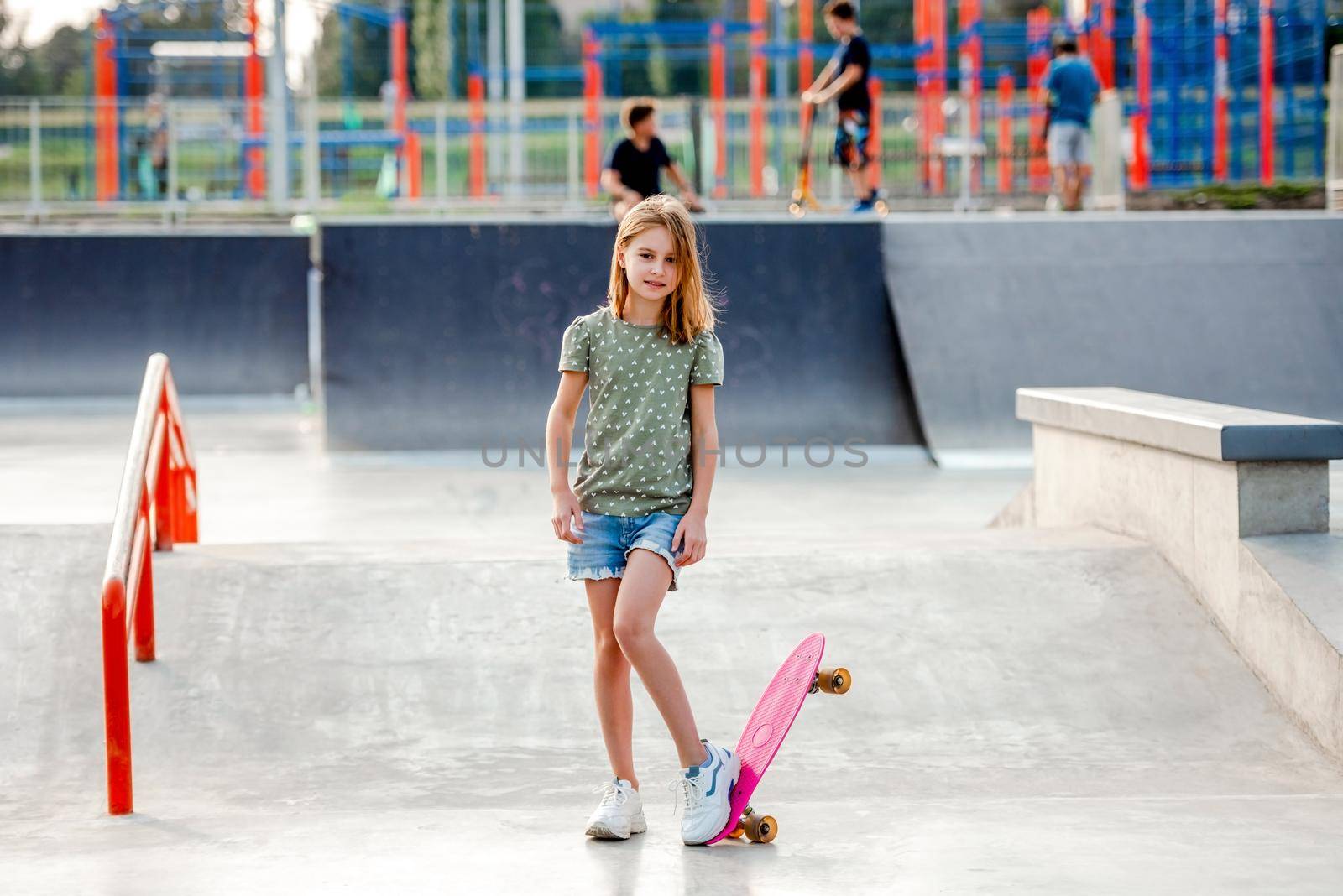 Pretty preteen girl with skateboard outdoors. Female skater child close to the park riding ramp