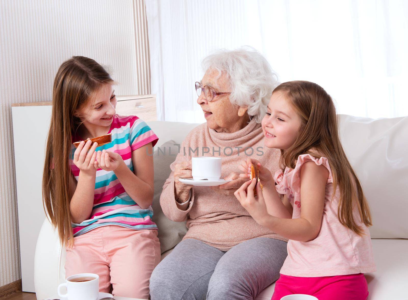 Smiling great-grandmother with granddaughters having tea