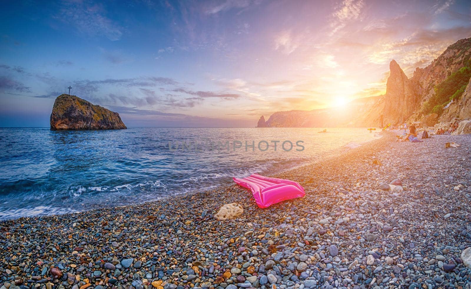 Pink inflatable mattress on the pebbles beach at sunset. Rocky seaside view with single inflatable mattress. Summer vacation background. Copy space. Travel, relax or loneliness concept