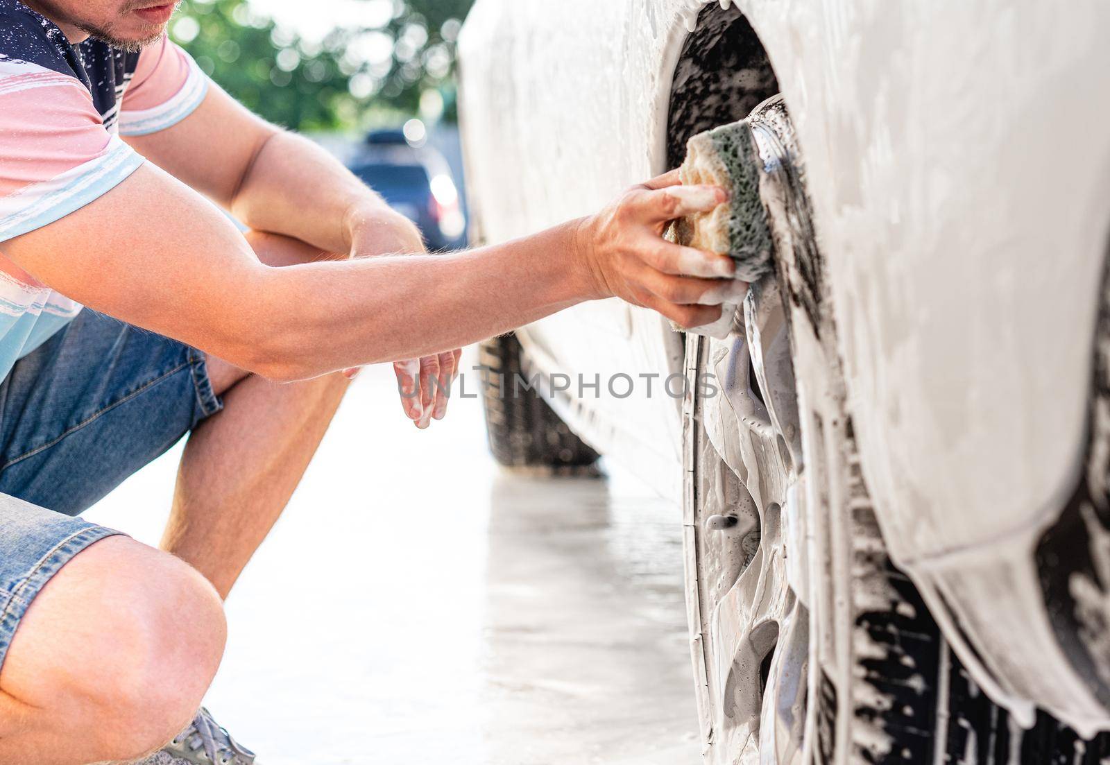 Man washing car's wheel with sponge and foam