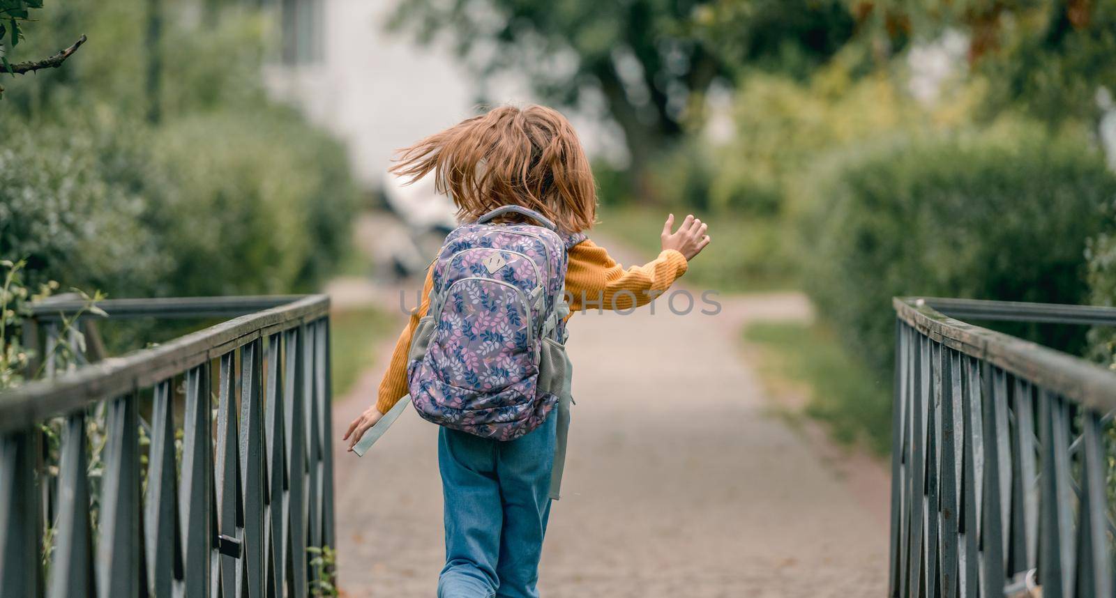 Little school girl with backpack outdoors portrait from back. Preteen child running in the park after lessons