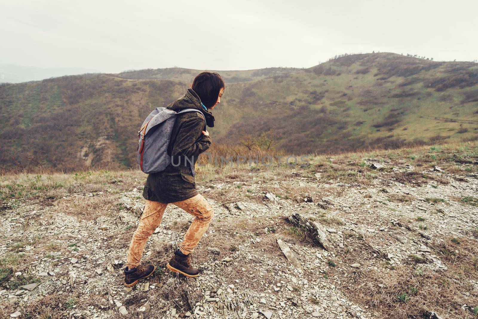 Hiker young woman with backpack walking in the mountains at rainy weather