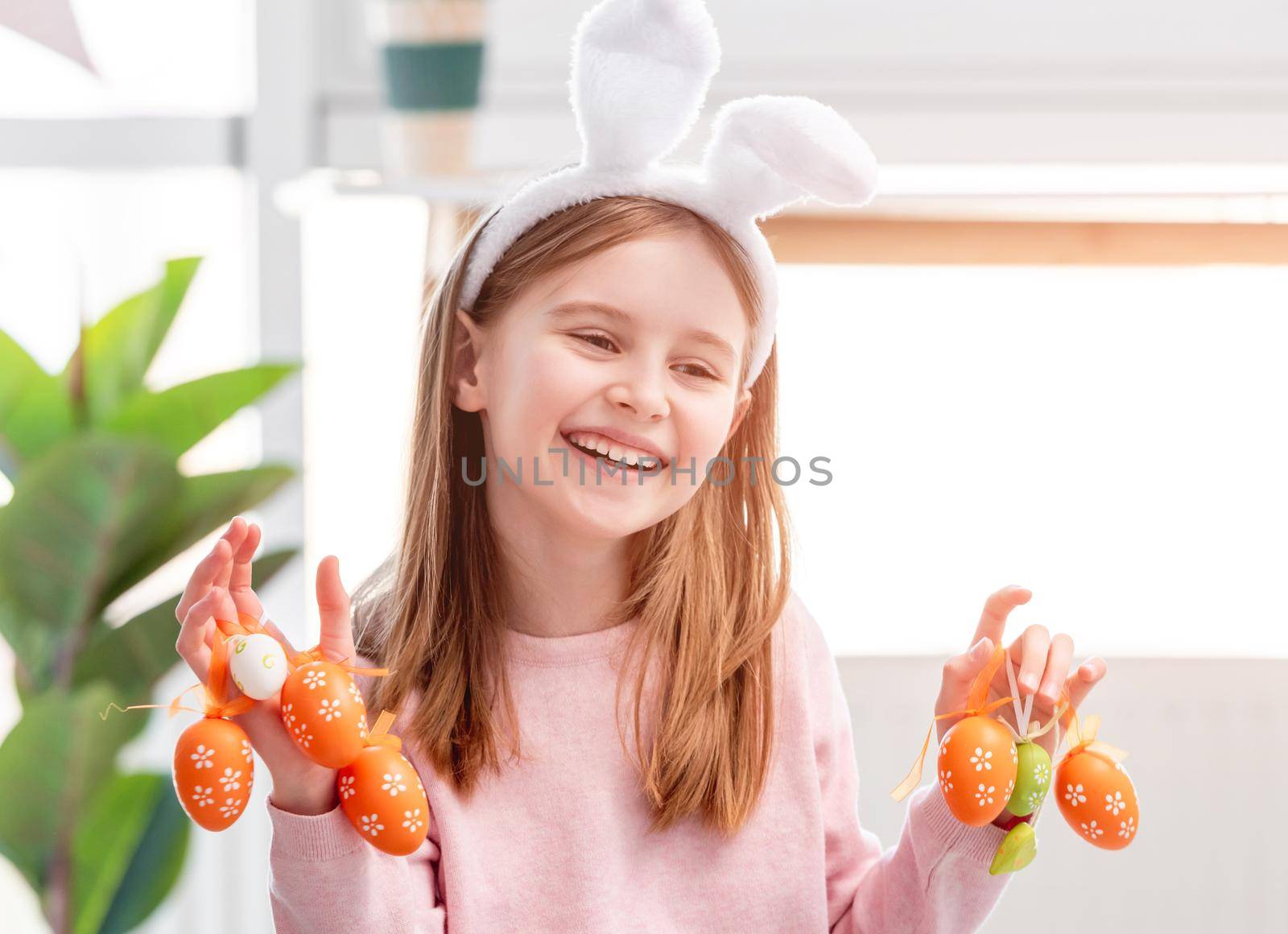 Beautiful portrait of cute little girl wearing bunny ears and holding painted Easter eggs in her hands