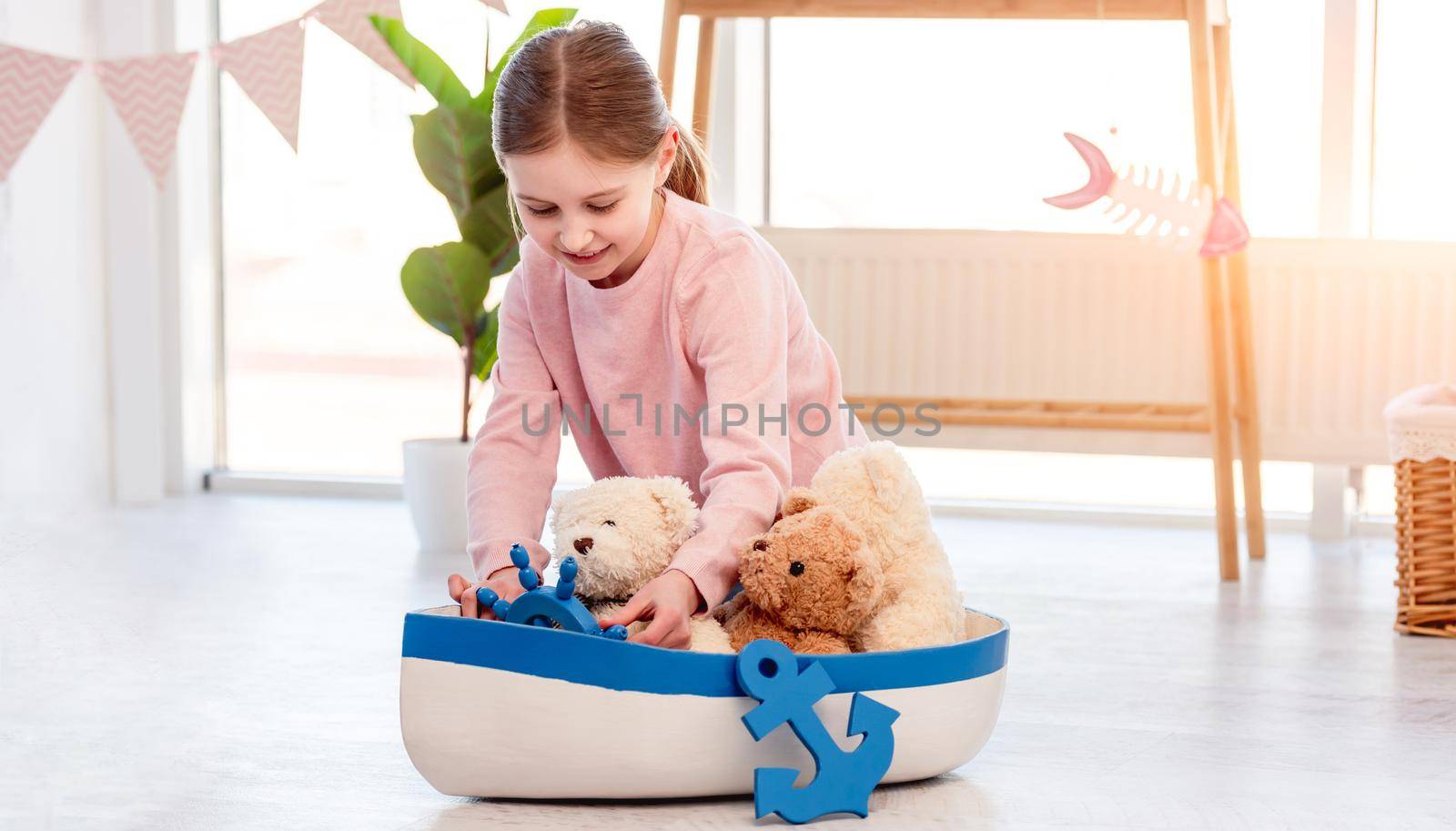 Little beautiful girl sitting on the floor and playing with toy ship in sunny room