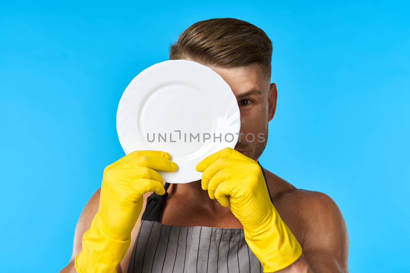 Dishwasher rubber gloves plate in hands blue background. High quality photo