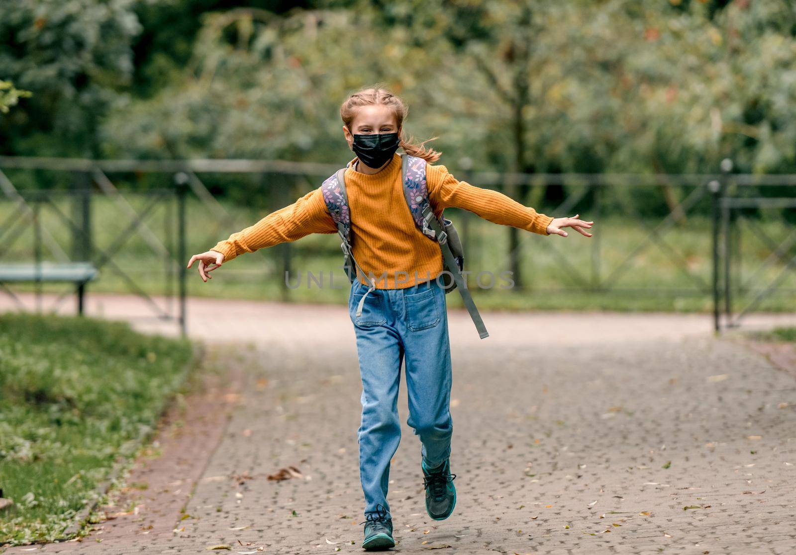 Preteen school girl with backpack wearing face mask running in the park after lessons. Carefree child kid at autumn outdoors in pandemic time