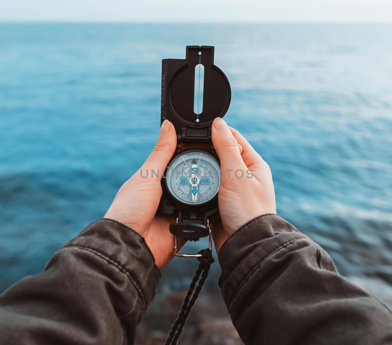 Tourist woman searching direction with a compass on stone coastline near the sea, close-up. Point of view shot.
