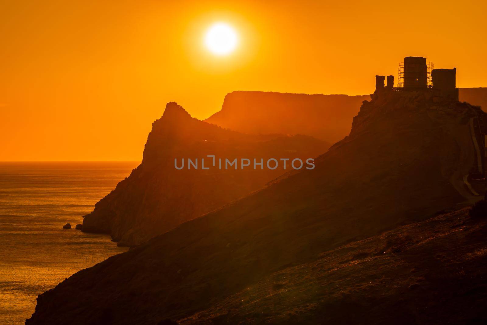 A red burning sunset with the silhouett of a cliff and castle over the sea