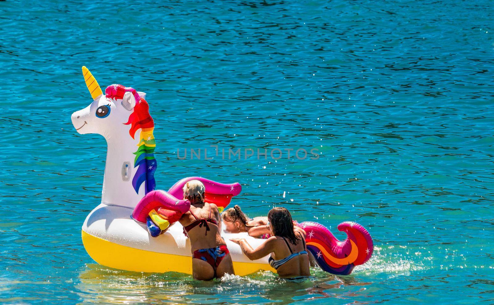 Family having fun on white unicorn at blue sea. Sunset holiday travel vacation background with funny unicorn toy float header as romantic Family background, summer family travel destination