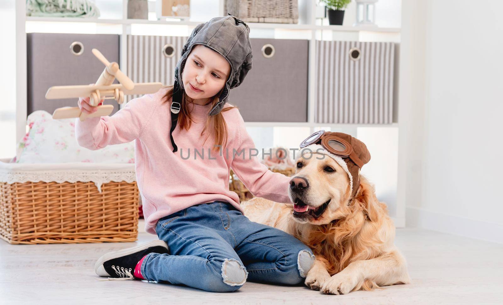 Little beautiful girl and golden retriever dog wearing pilot costumes playing games with wooden plain