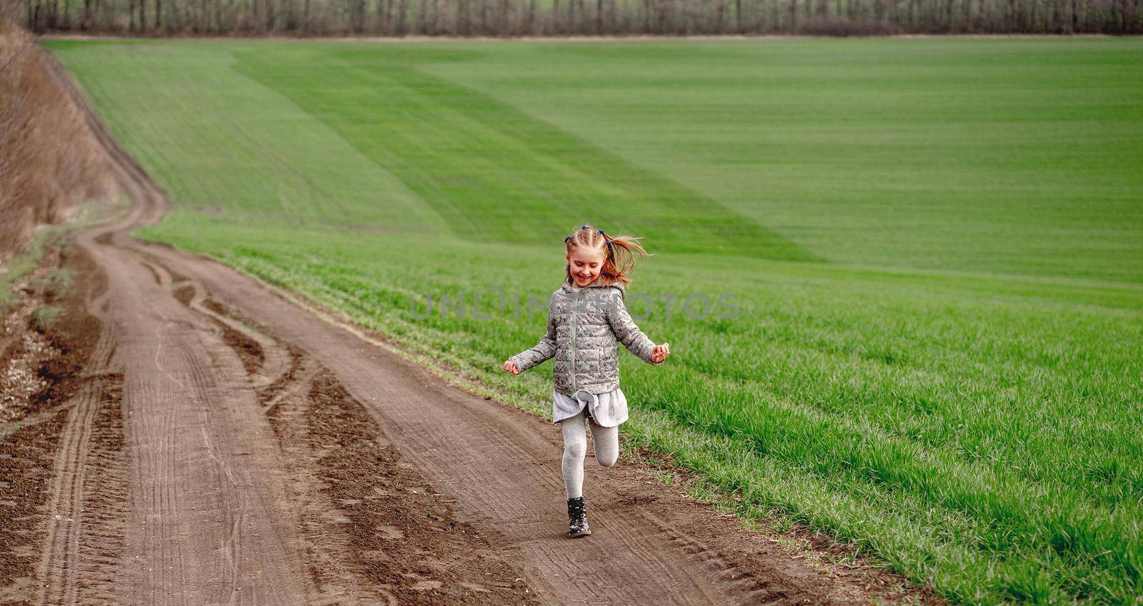 Happy little girl running along path on green spring field