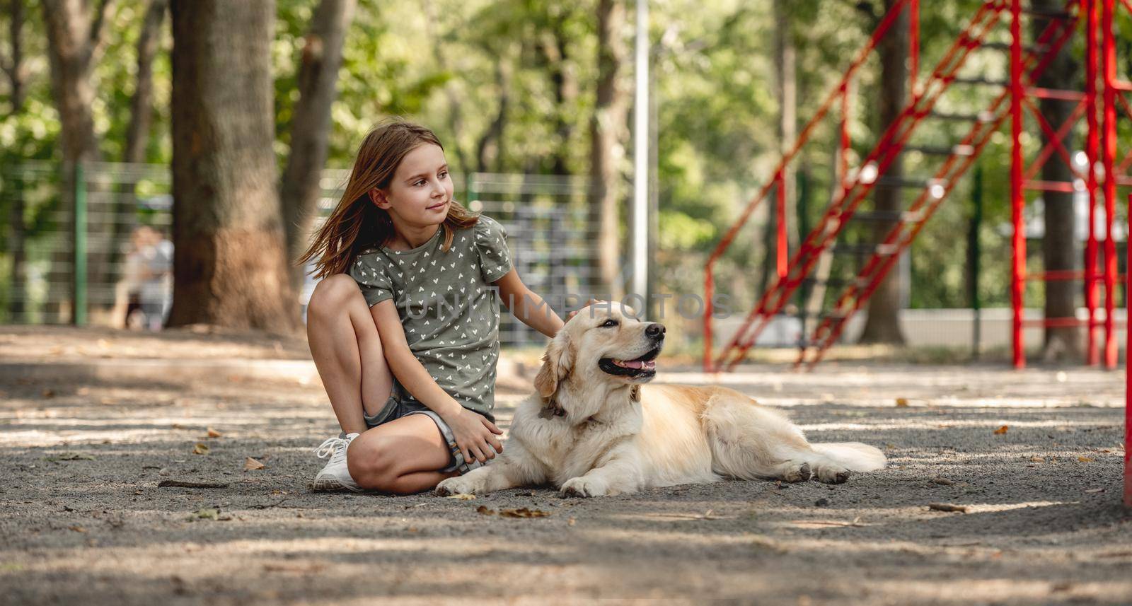 Preteen girl with golden retriever dog sitting on the earth in the park. Cute child with doggy pet portrait outdoors