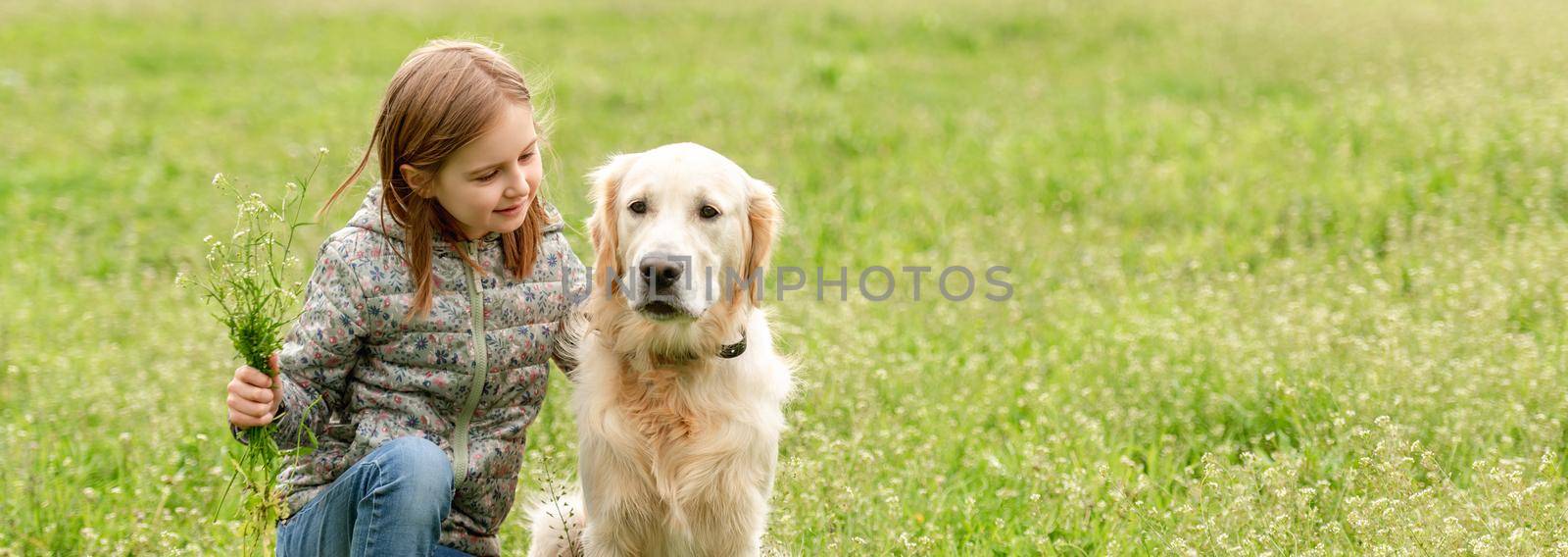 Smiling little girl looking at cute dog sitting in flowers on sunny field