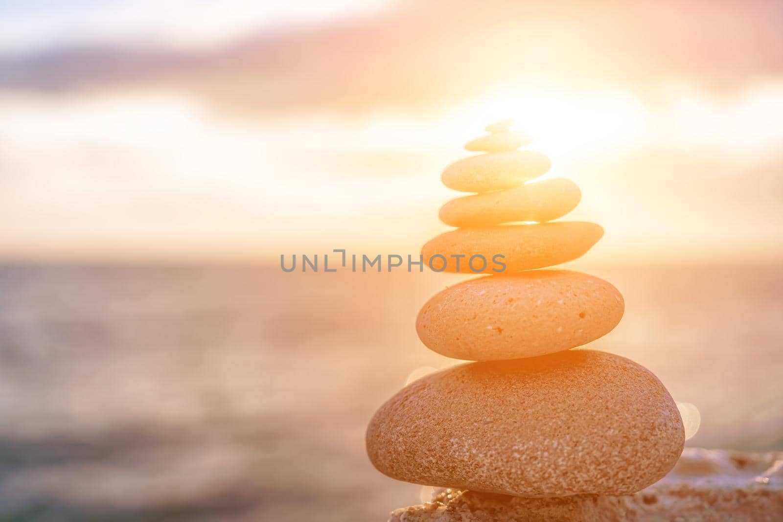 Balanced rock pyramid on the pebble beach on sunset. Selective focus Abstract bokeh from Sea foam on the background. Zen stones on the sea beach, meditation, spa, harmony, calmness, balance concept by panophotograph