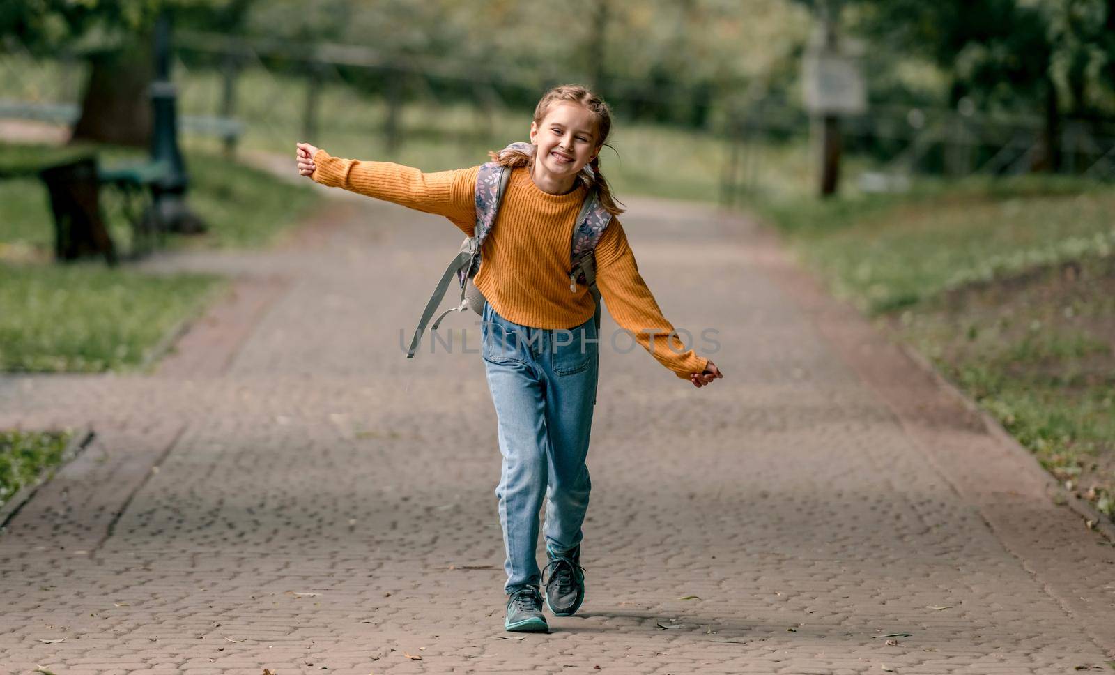 Pretty school girl with backpack running in the park after lessons. Sweet child kid at autumn outdoors