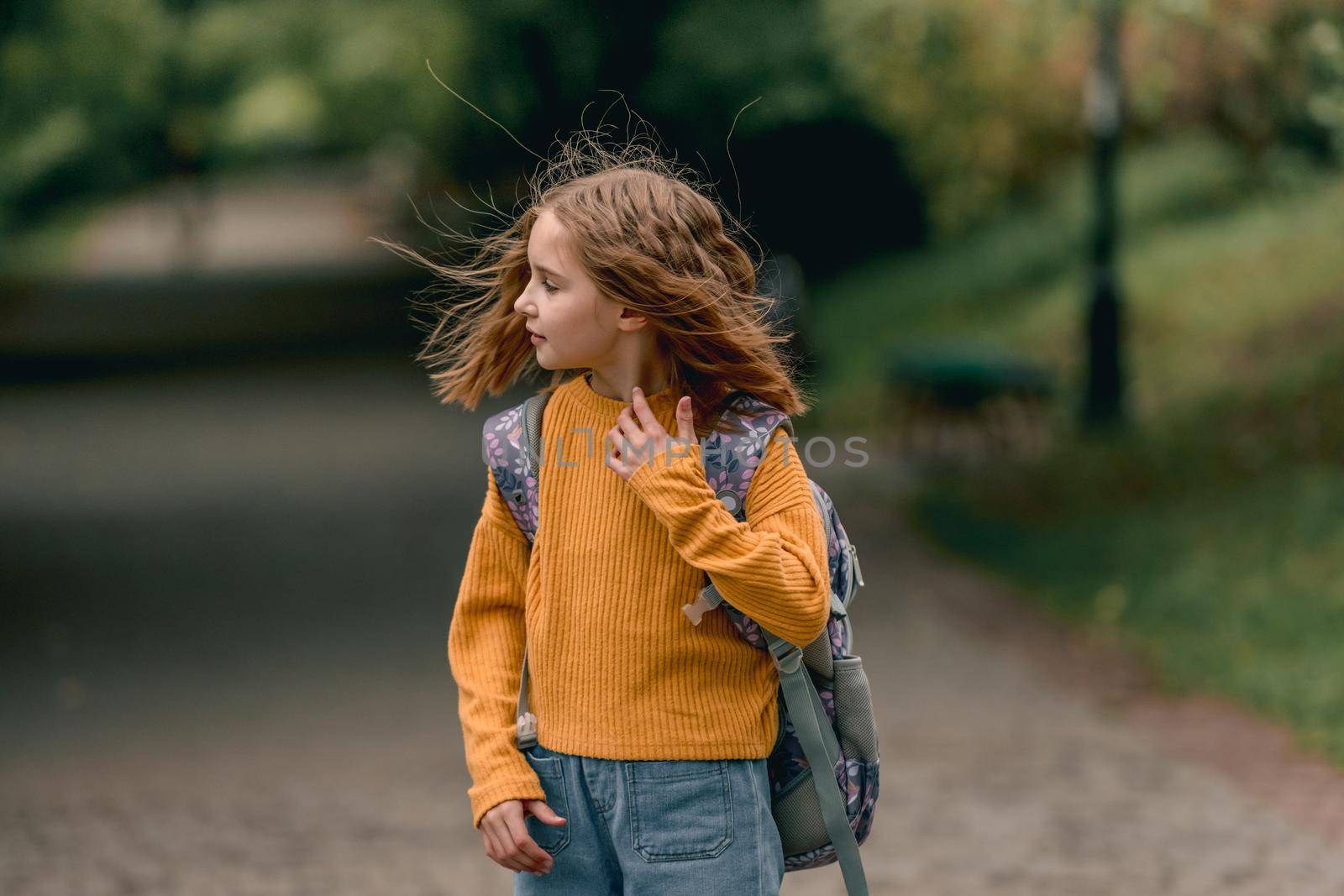 Beautiful girl child with back pack after school looking back at the street at autumn. Portrait of preteen female kid outdoors