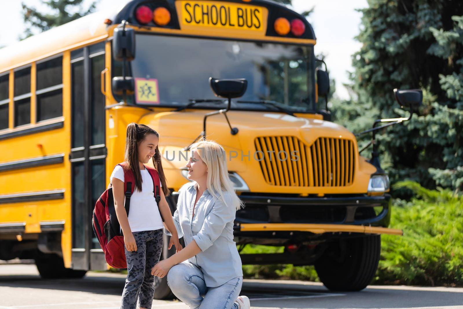 Mother escorts the schoolgirl with ponytails and a backpack to school.