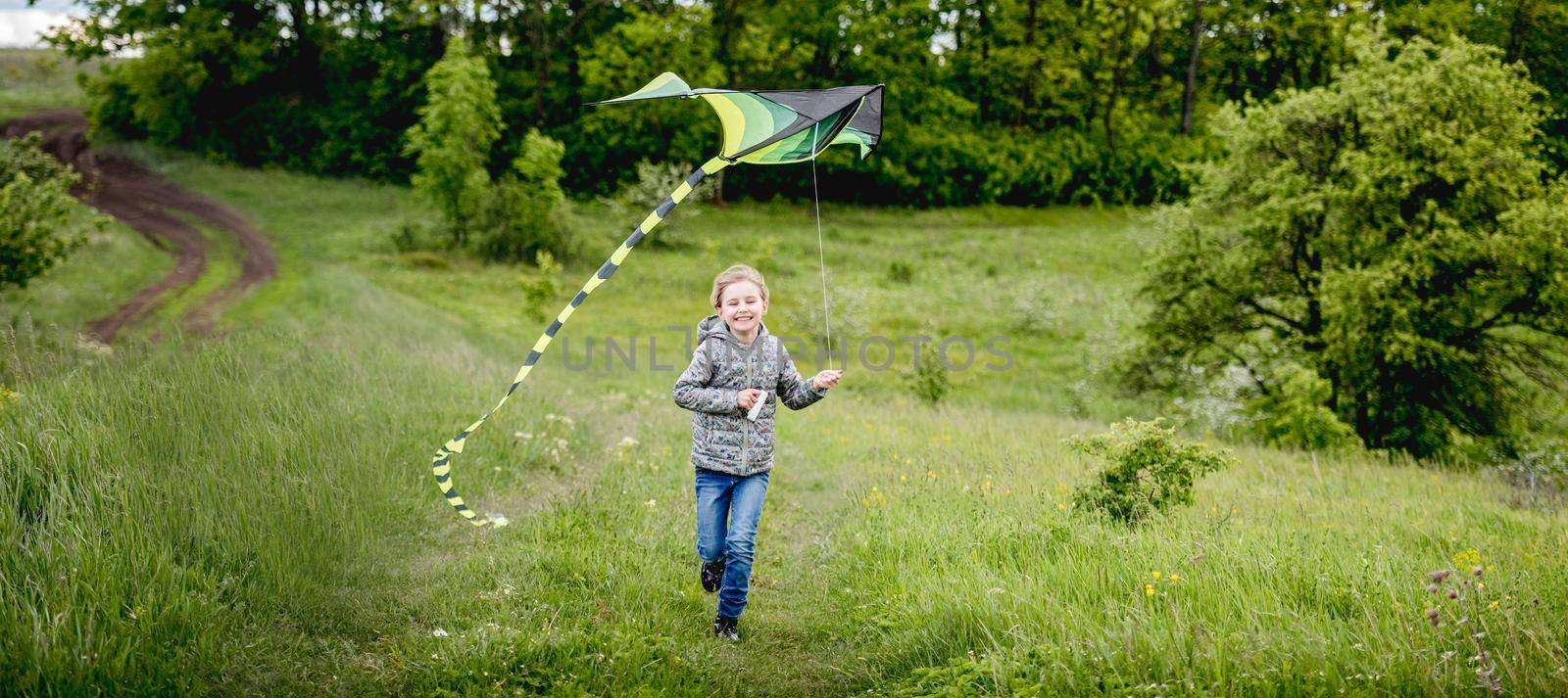 Happy little girl flying bright kite outdoors on nature in spring