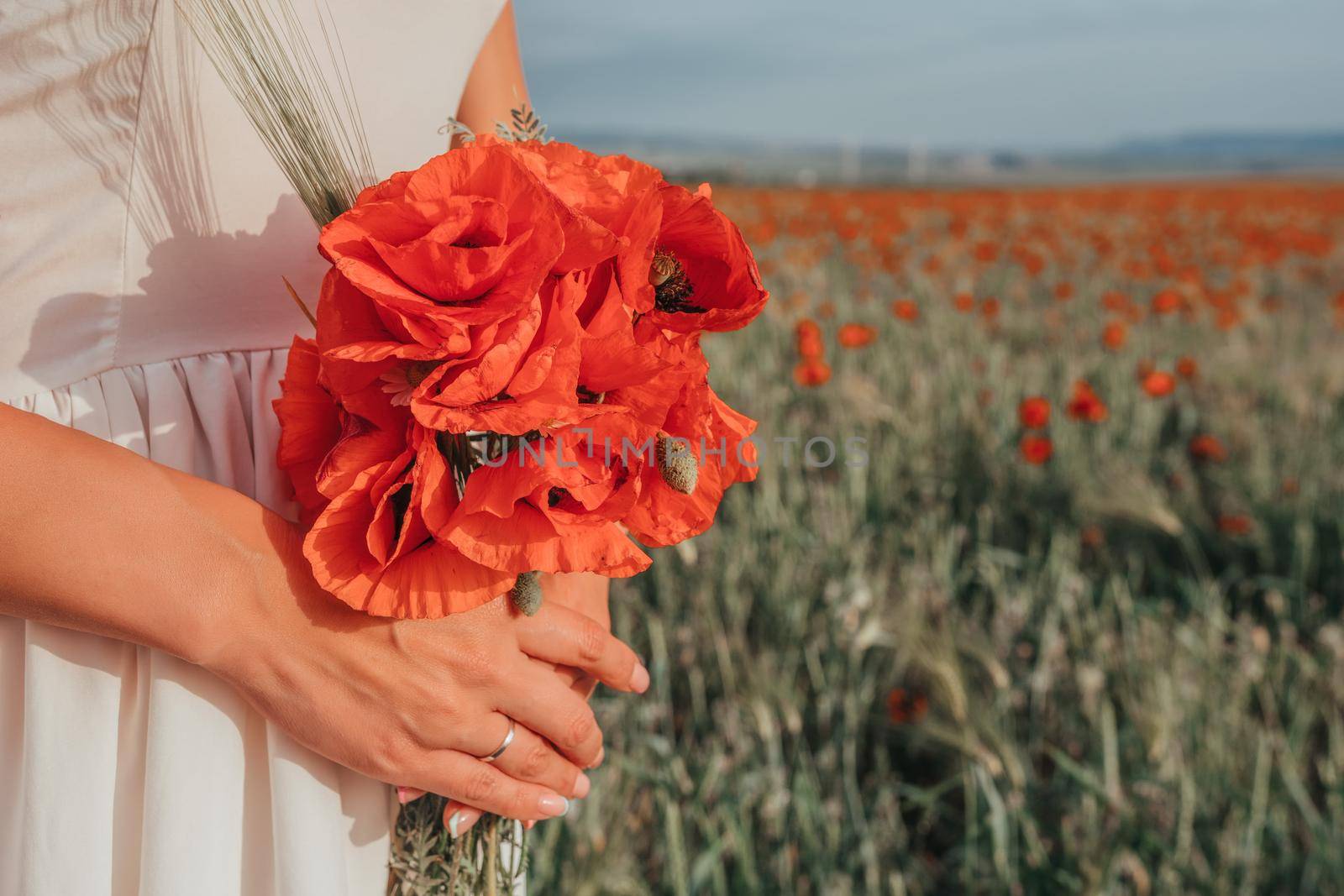 Bride in a white dress holding a bouquet of poppy flowers, warm sunset time on the background of the lavender field. Copy space. The concept of calmness, silence and unity with nature.