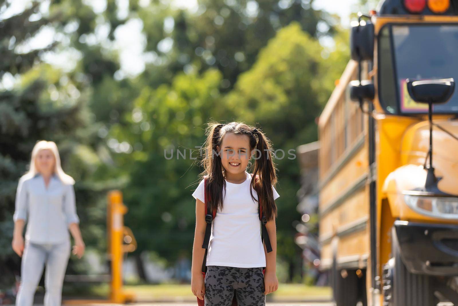 Mother brings her daughter to school near the school bus. back to school