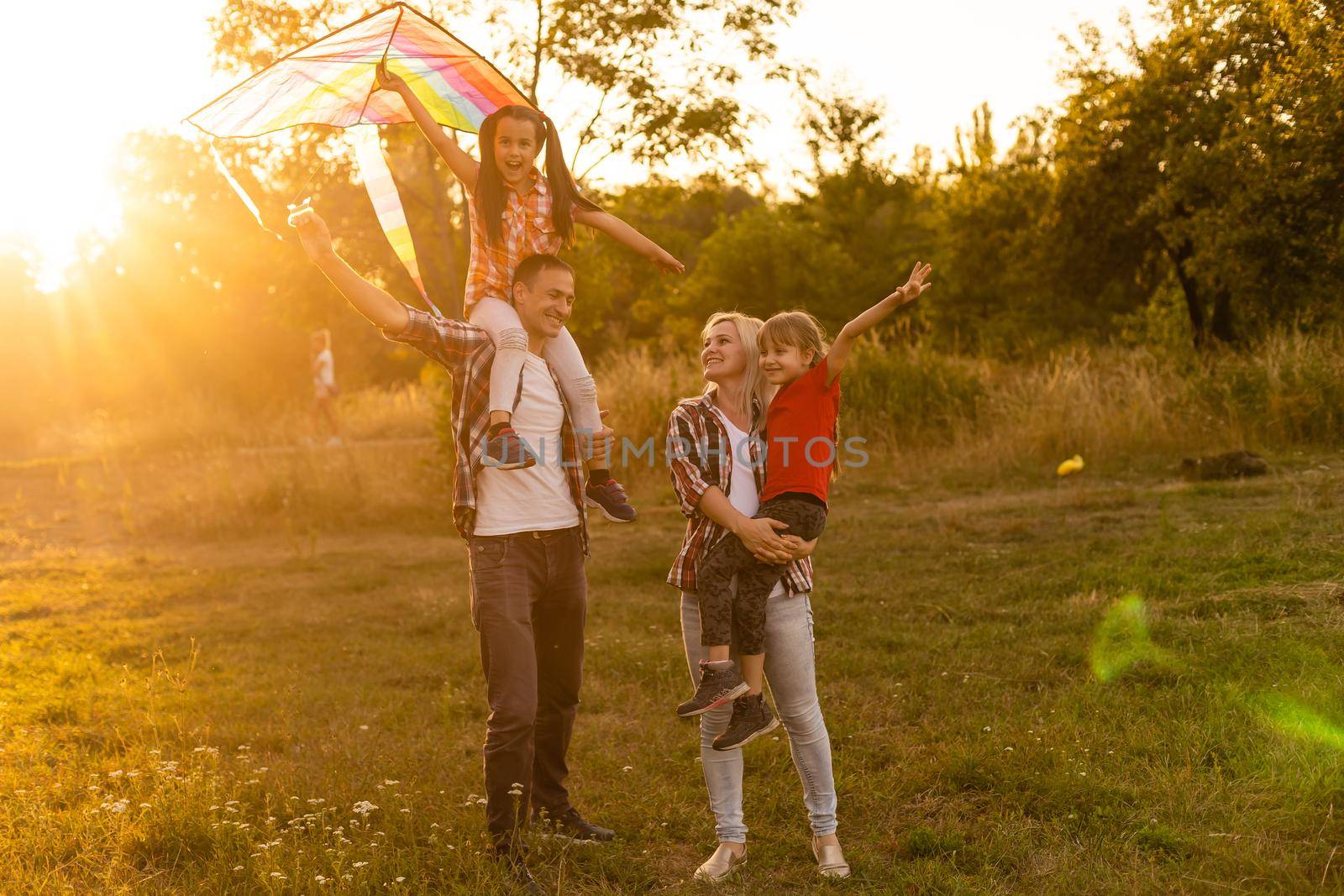 Happy family with a kite playing at sunset in the field by Andelov13