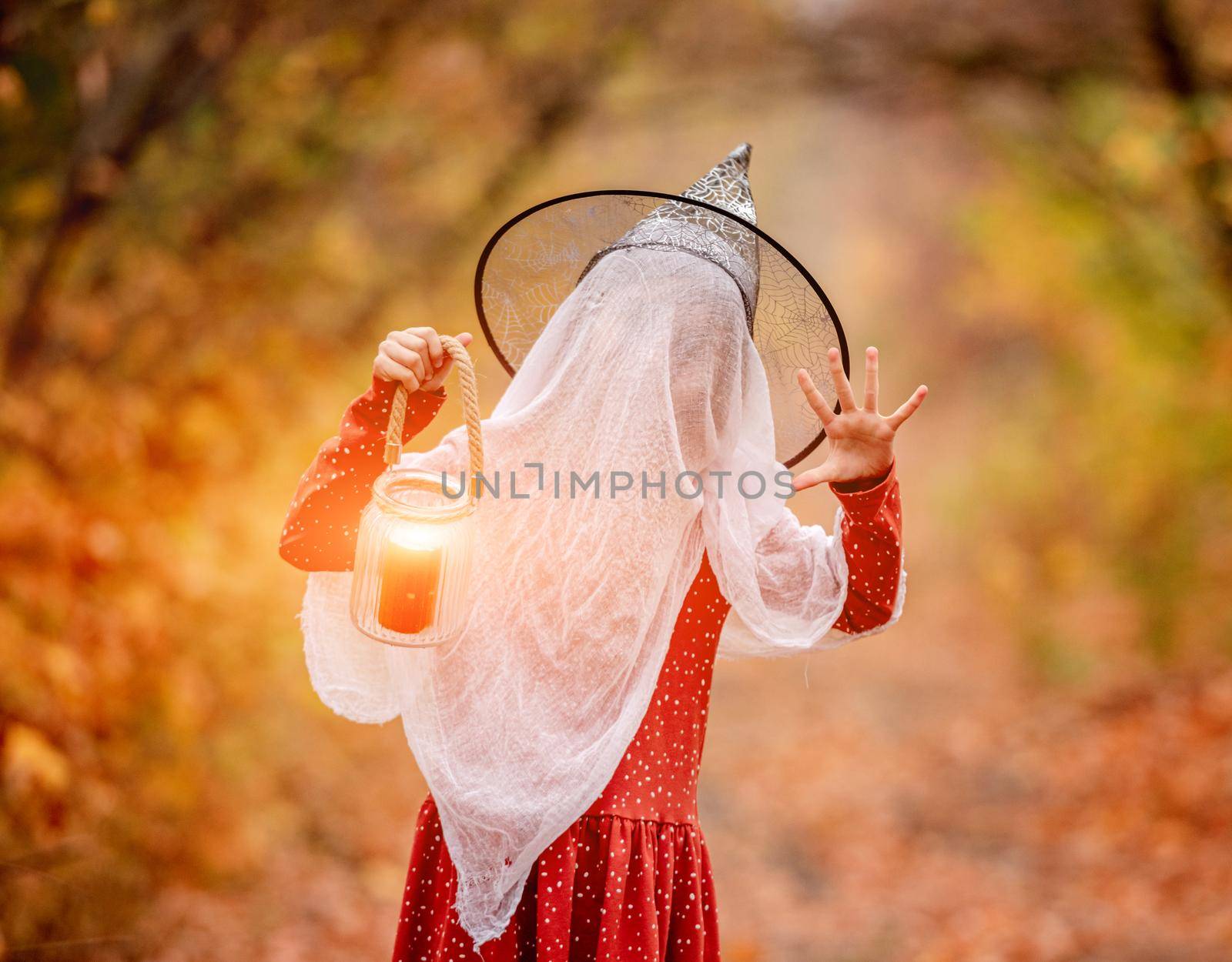 Little girl in halloween costume with candle frighting on autumn nature background