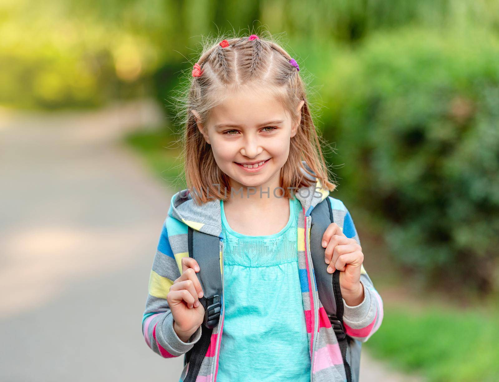 Little girl with backpack going to school through park alley