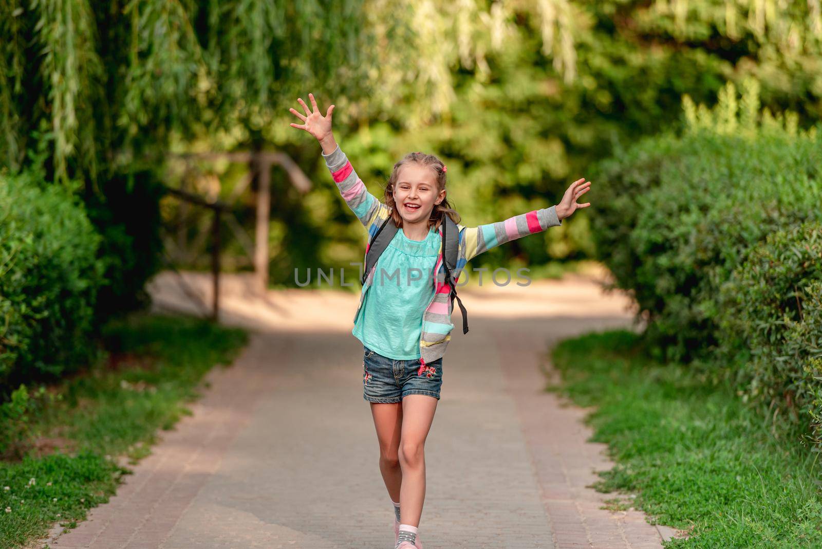 Little girl with backpack going home after school along park road