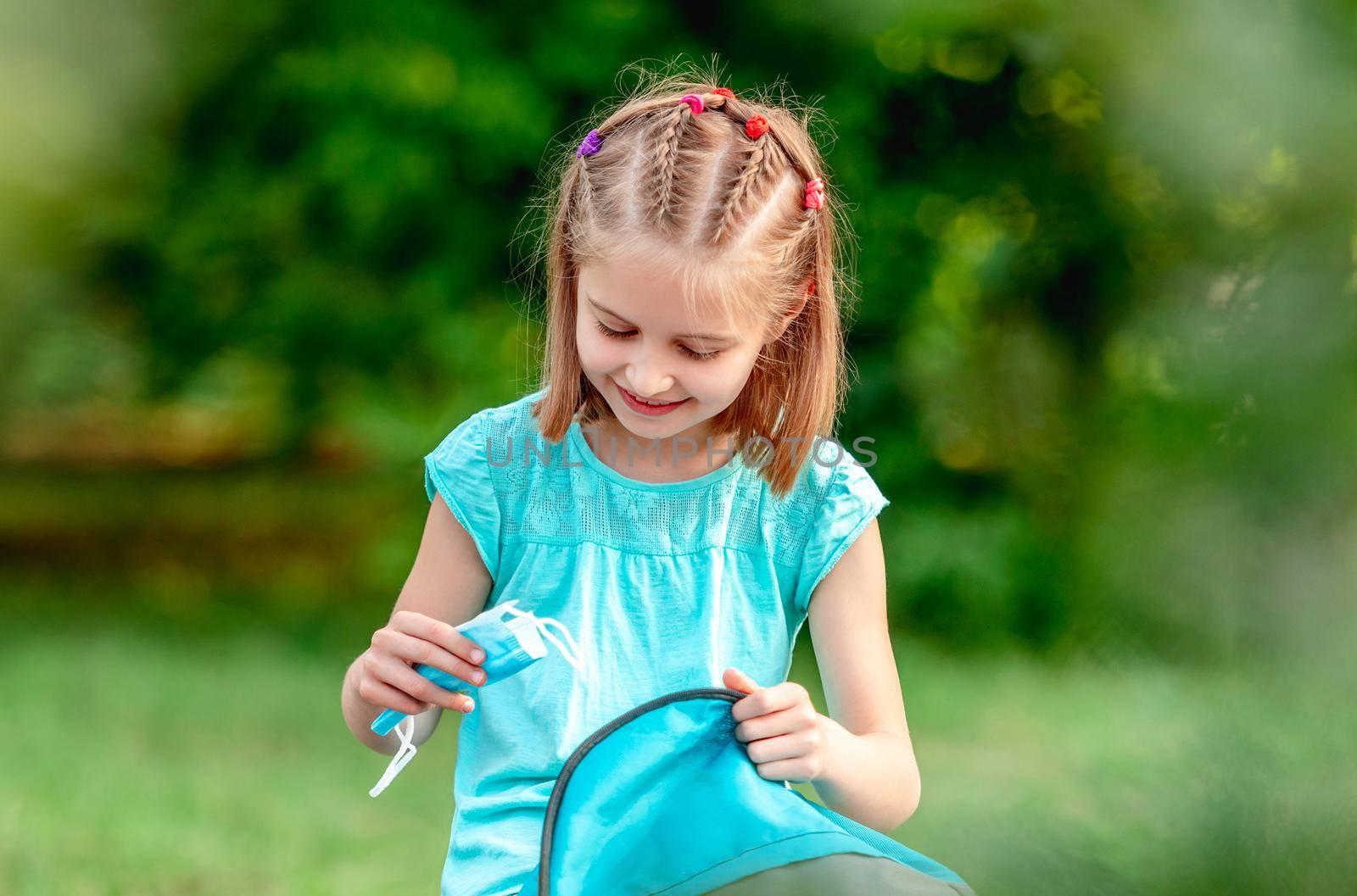 Little girl taking out medical mask from backpack in park