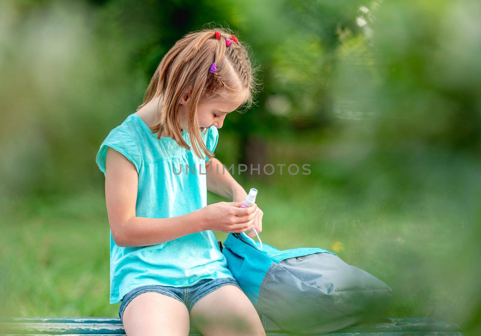 School girl with sanitizer sitting on bench in park