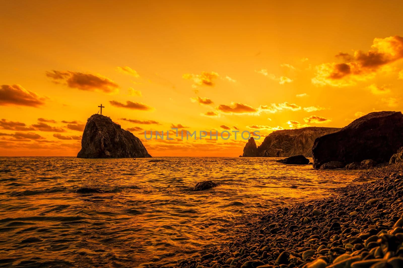 A red burning sunset on pebble beach with the silhouette of a cliff over the sea. Copy space. The concept of calmness, silence and unity with nature. cape Fiolent, Sevastopol, Crimea.