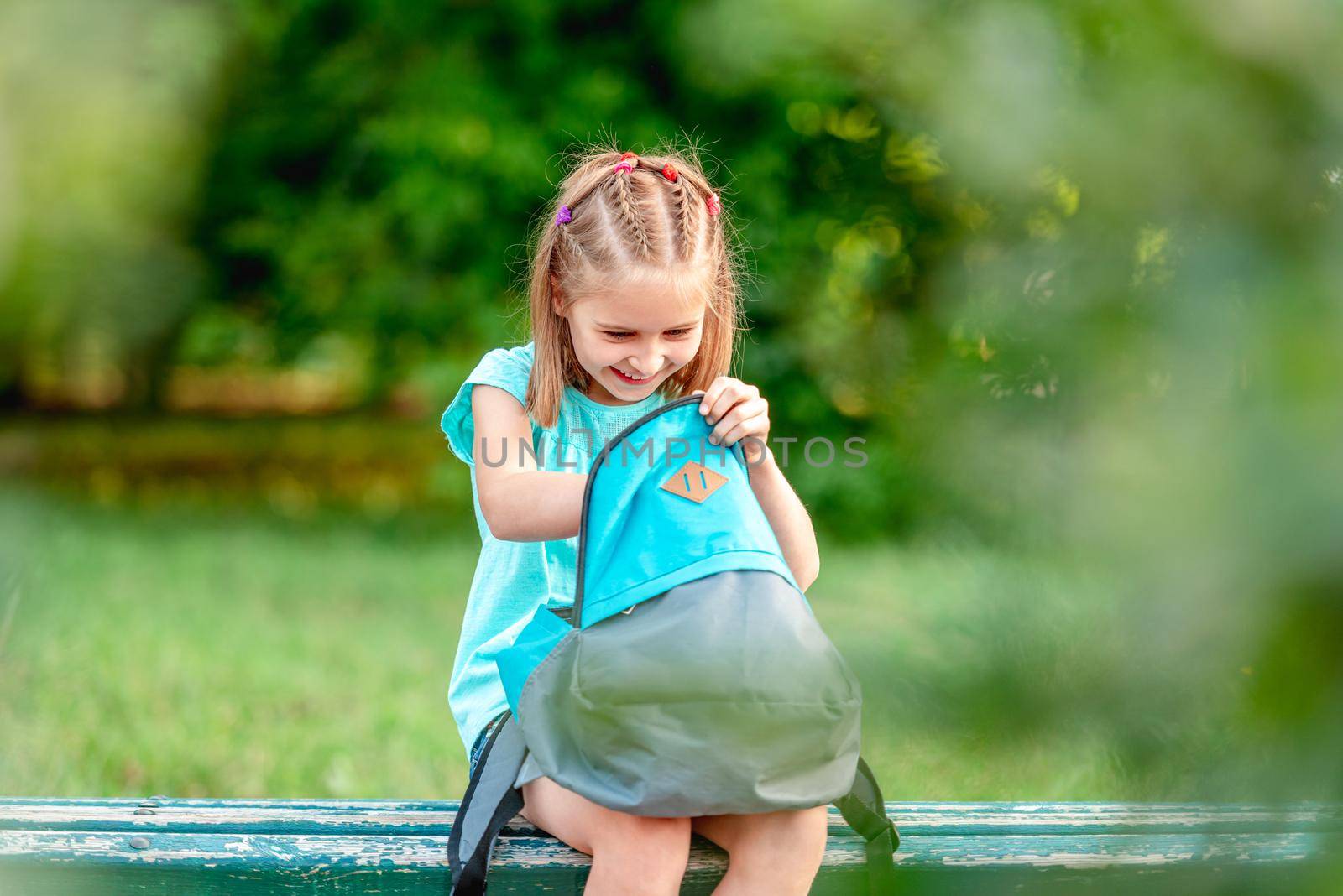 Schoolgirl peeking into backpack in park by tan4ikk1