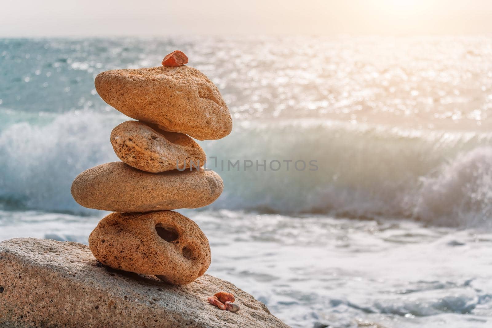 Balanced pebble pyramid on the beach on a sunny day. Sea foam on the background. Selective focus. Zen stones on the sea beach, meditation, spa, harmony, calmness, balance concept by panophotograph