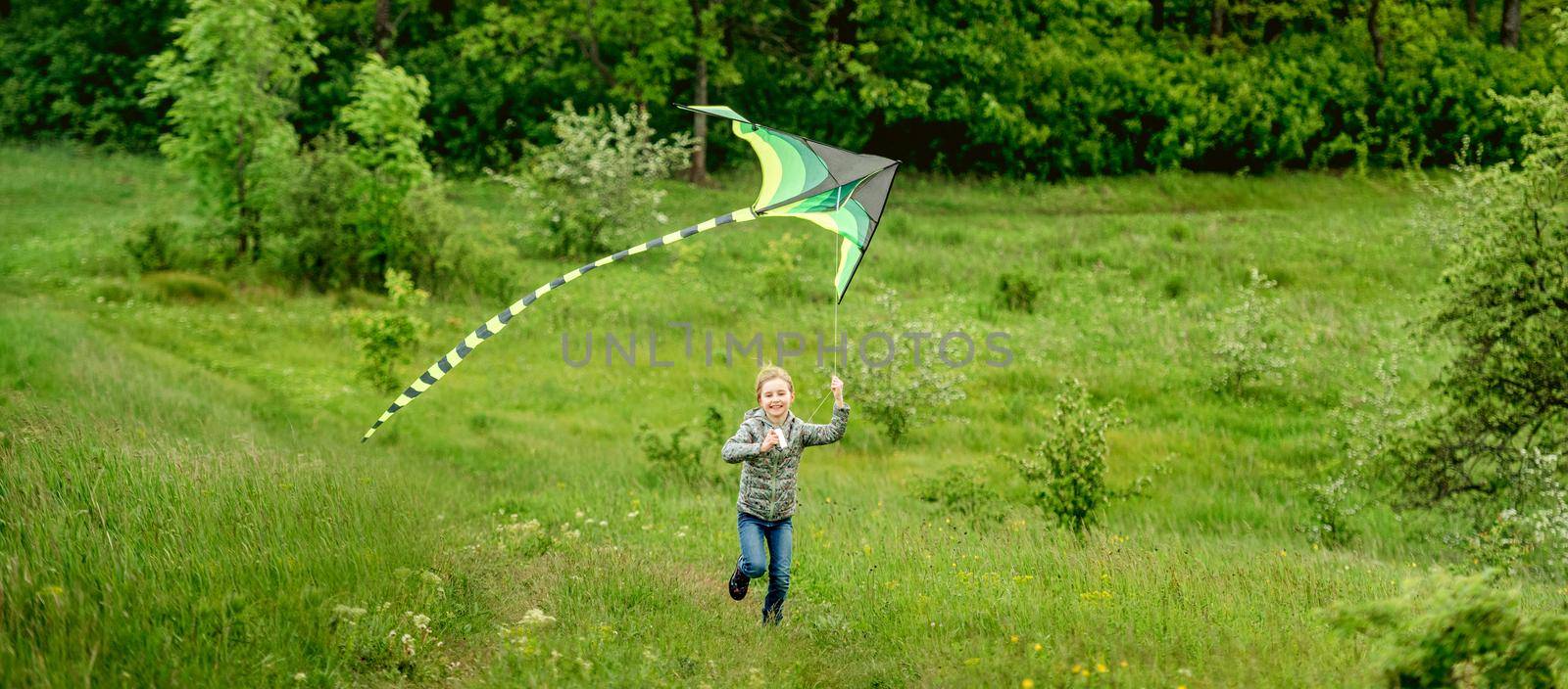 Happy little girl flying bright kite outdoors on nature in spring