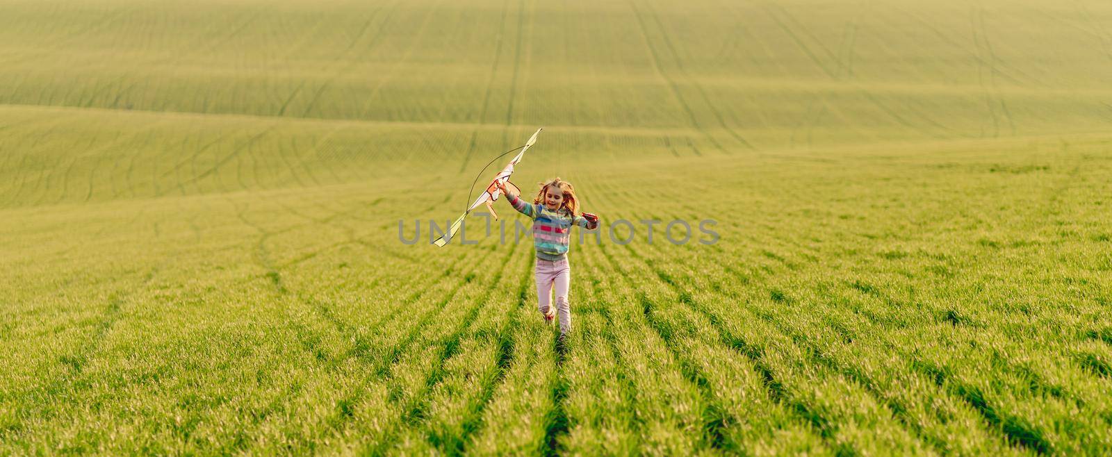 Beautiful little girl playing with kite on juicy green field